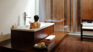 A modern bathroom with a wooden floor, a bathtub, a shower area, and a wooden bench. - COMO Metropolitan Bangkok (Bangkok)
