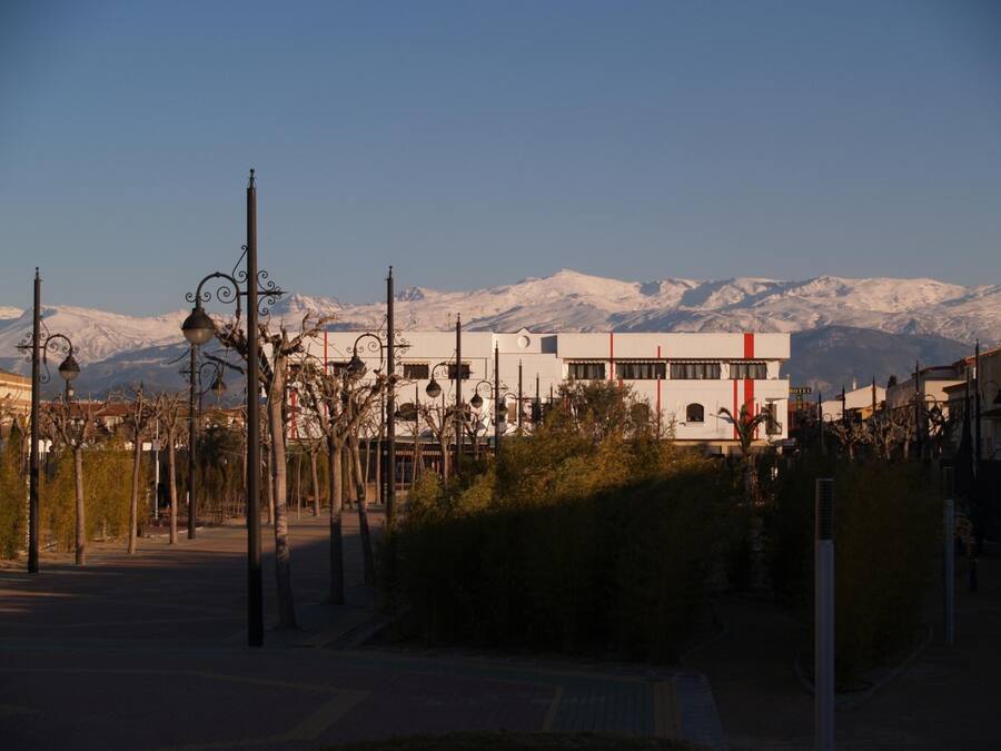 Un hotel de diseño moderno, con una llamativa banda roja en la fachada, ubicado en un pueblo con montañas nevadas al fondo.
