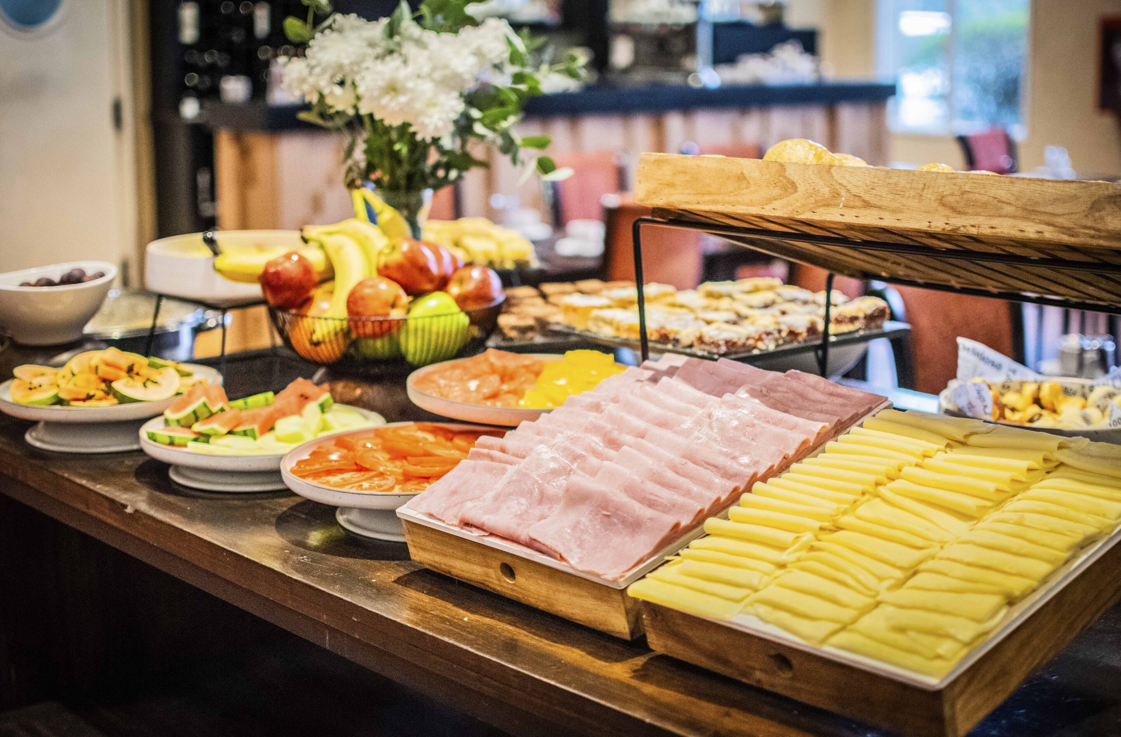 A buffet with various food items including sliced meats, cheeses, and fruits.