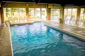 An indoor swimming pool with clear water, surrounded by chairs and large windows offering views of a landscaped area. - Wyndham Garden Campana (Campana)