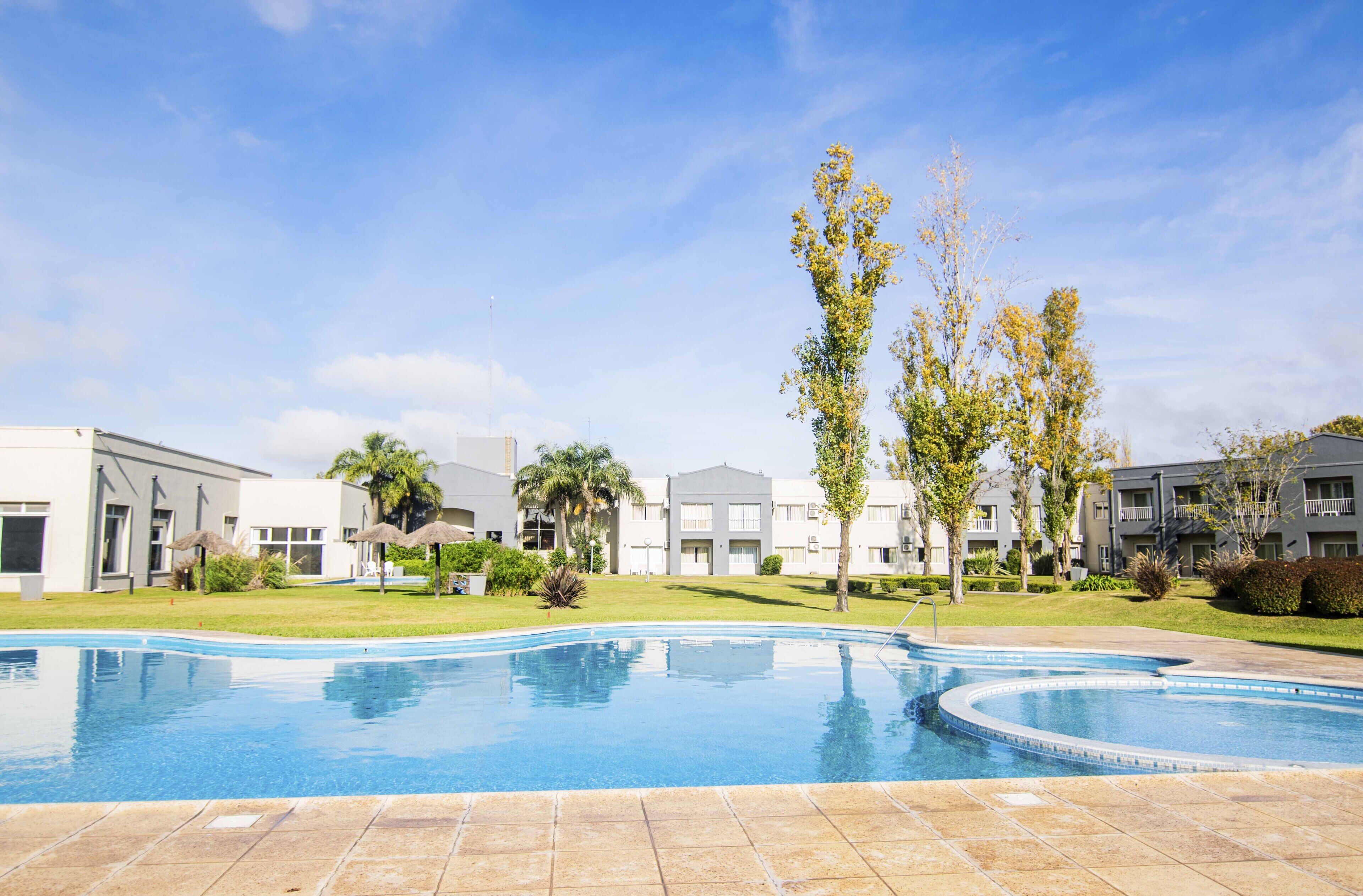 Una piscina con solárium empedrado, rodeada de edificios con balcones y un cielo despejado.