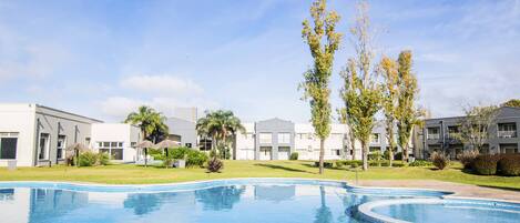 Una piscina con solárium empedrado, rodeada de edificios con balcones y un cielo despejado.