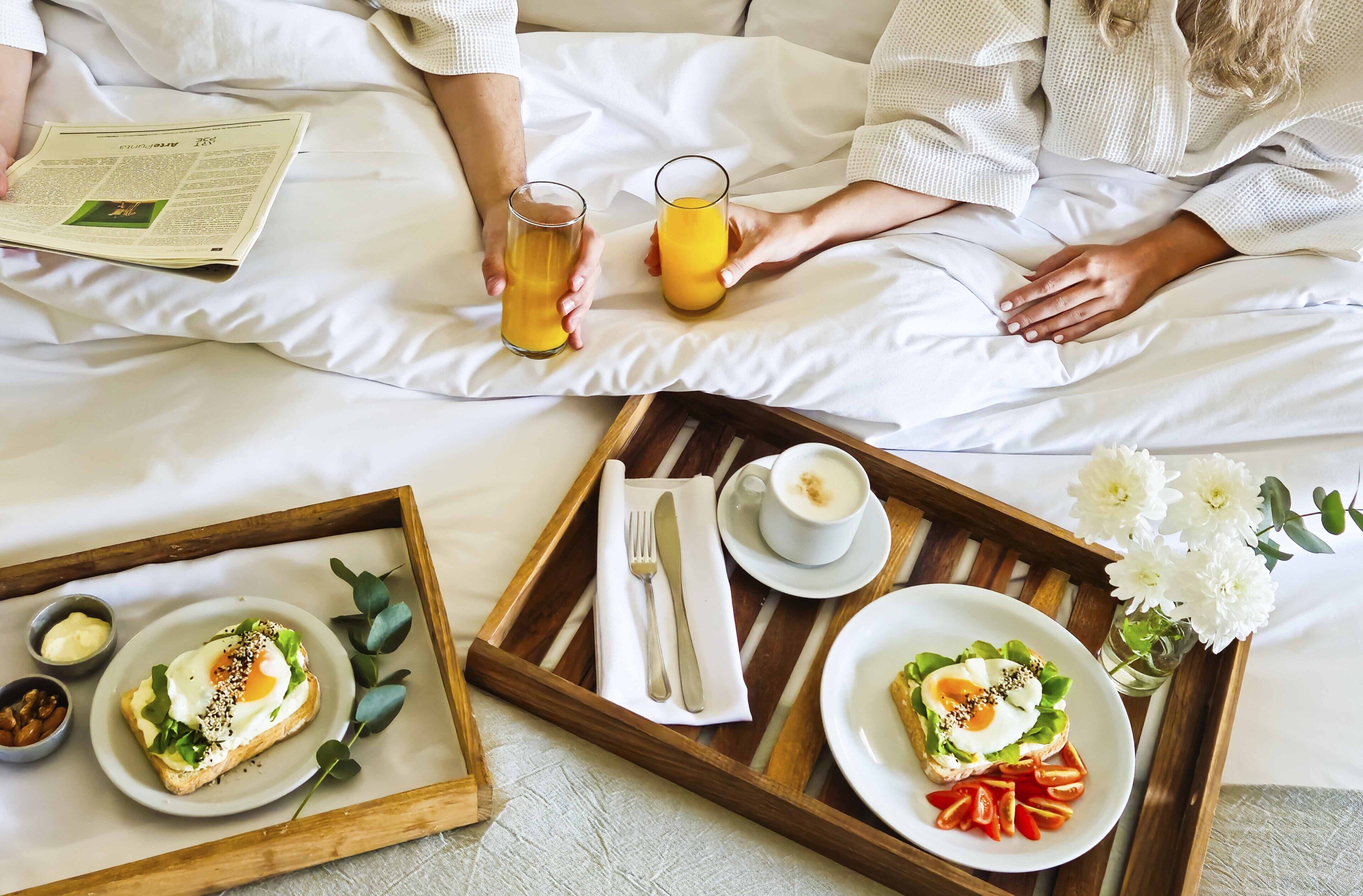 A breakfast tray with toast, eggs, and tomatoes on a bed with white bedding.
