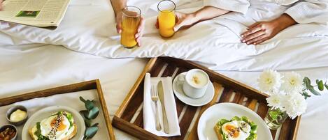 A breakfast tray with toast, eggs, and tomatoes on a bed with white bedding.