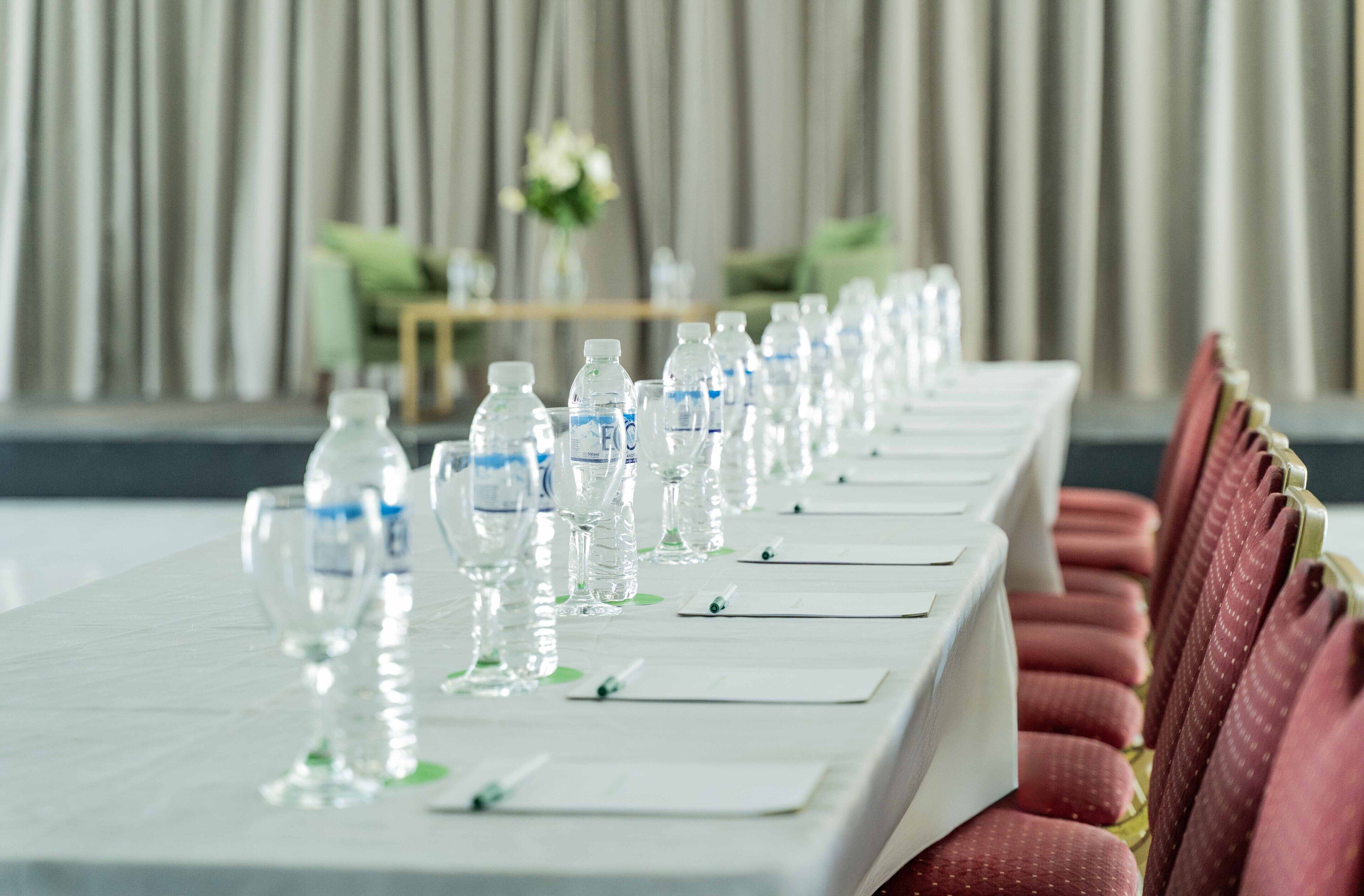 Mesa de conferencias preparada con botellas de agua, vasos y blocs de notas, señal de una disposición para reunión o evento.