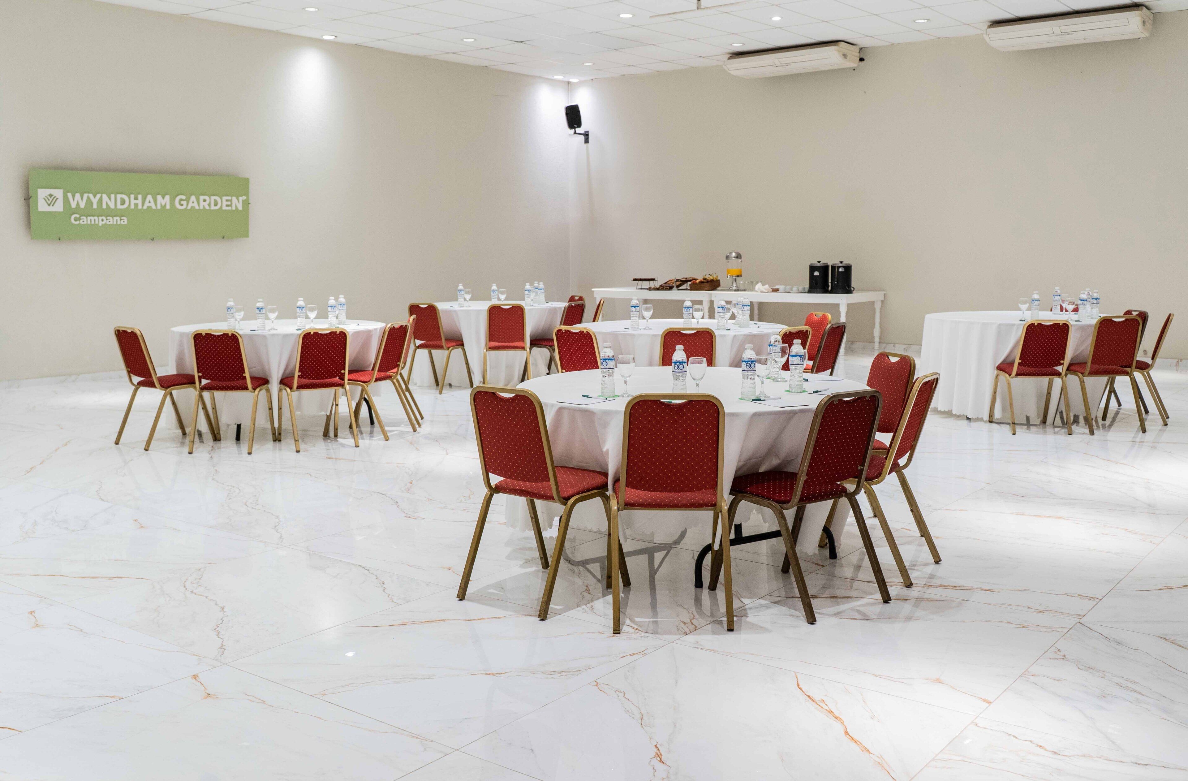 A conference room with round tables and red chairs, water bottles, and a speaker on the wall.