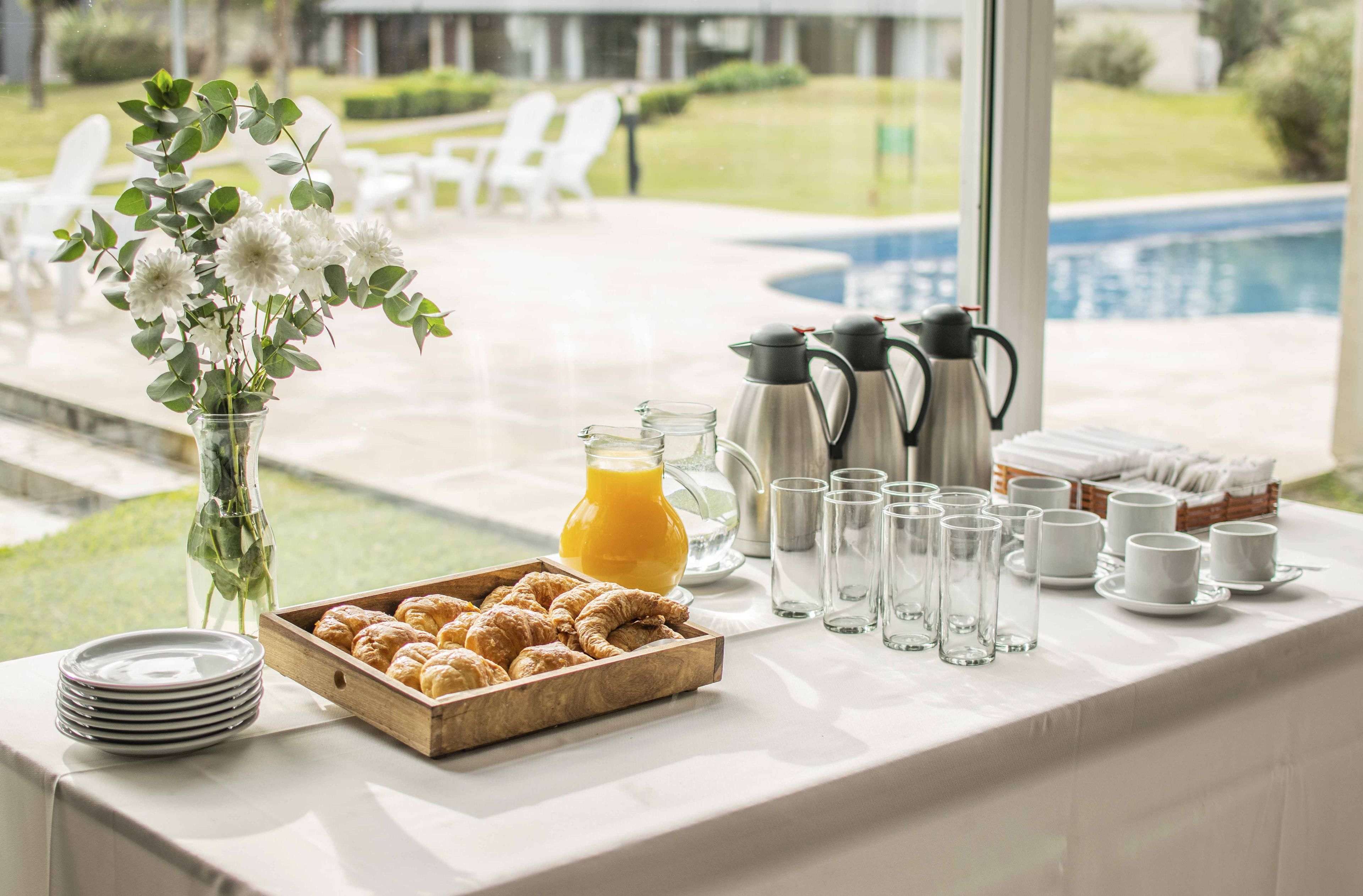 A breakfast buffet setup with croissants, juice, coffee pots, and cups.