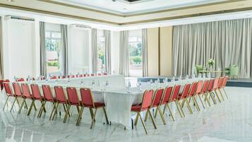 Un salón de conferencias con una larga mesa, sillas rojas y vistas a un jardín a través de amplios ventanales.