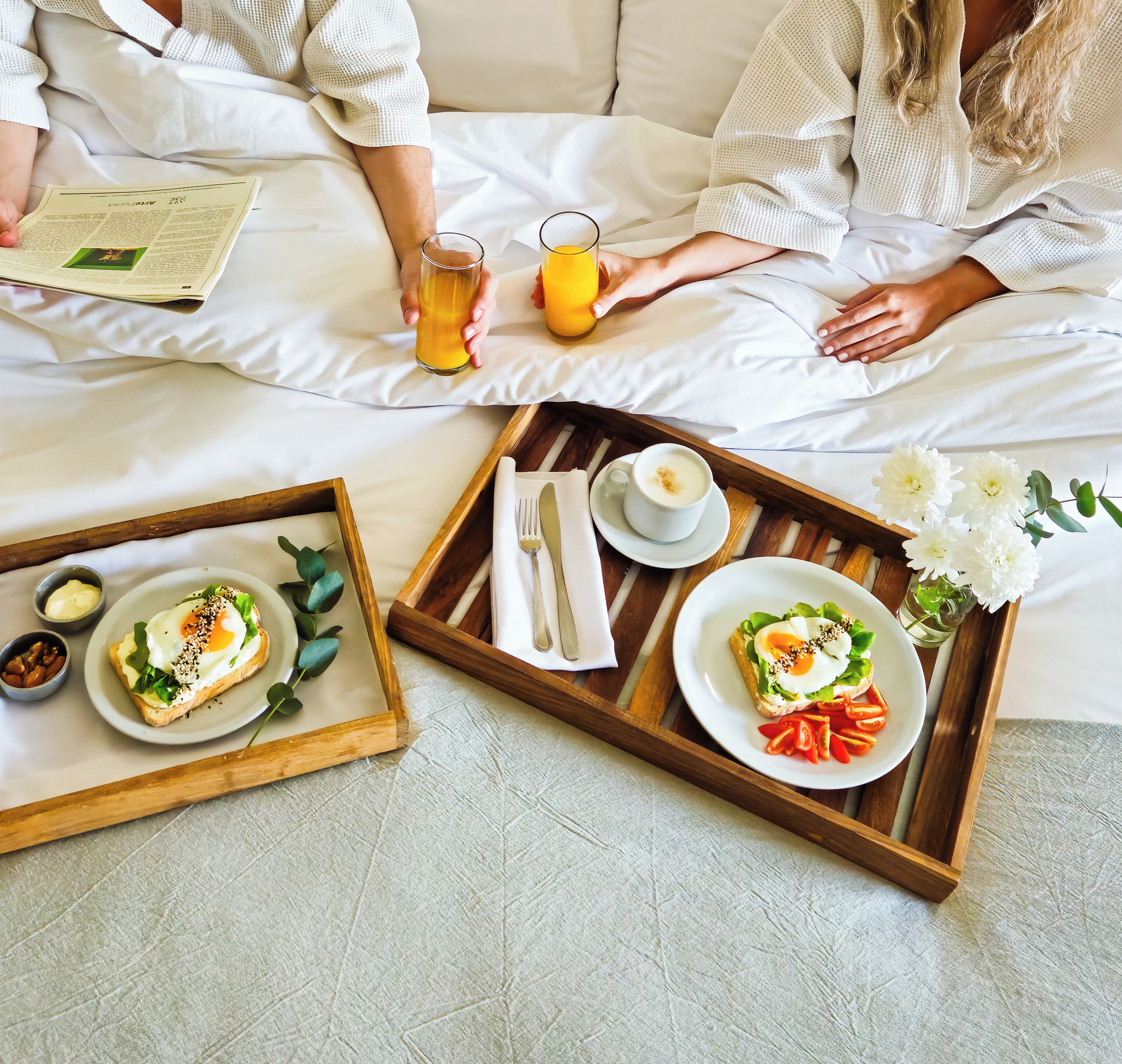 Bandeja de desayuno con tostadas, huevos y tomates sobre una cama.
