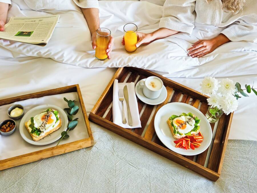 Un vassoio per la colazione con pane tostato, uova e pomodori su un letto.