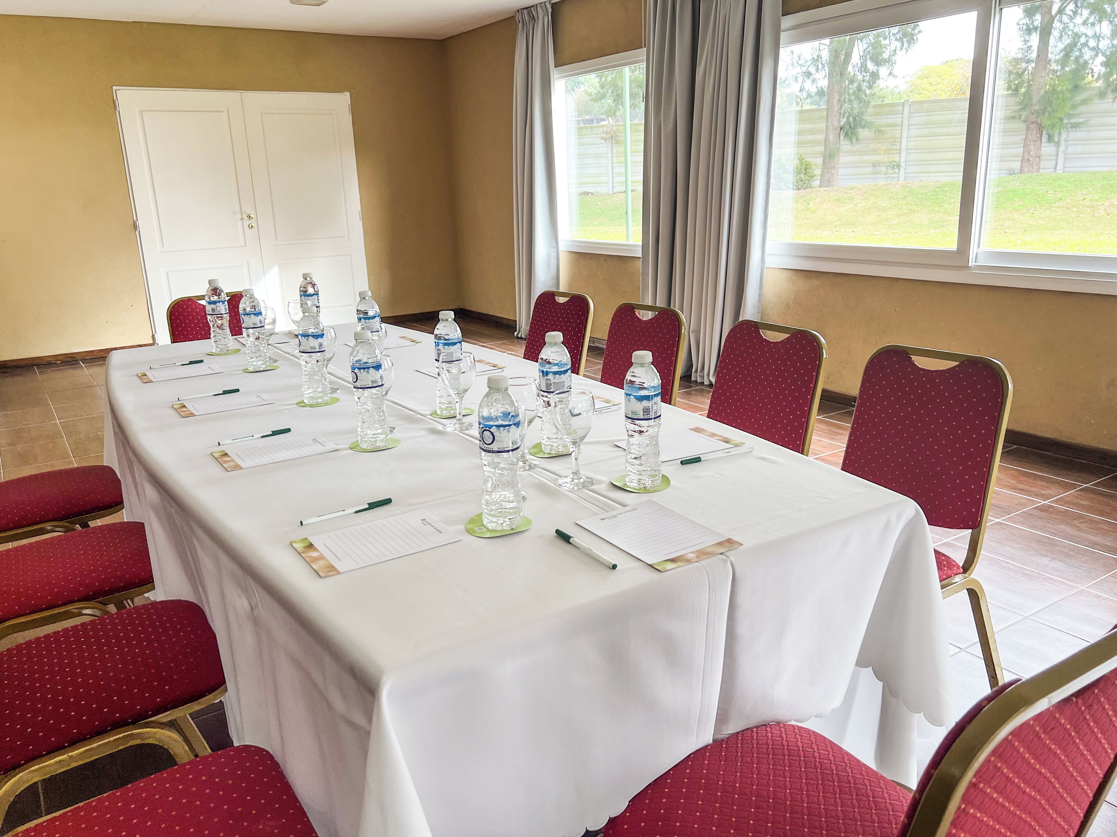 A conference room with a long table set for a meeting, red chairs, and a whiteboard on the wall.