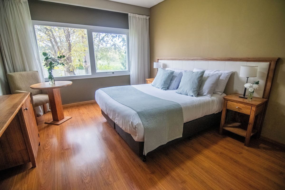 A neatly arranged bedroom with a bed, bedside tables, a chair, and a small table.