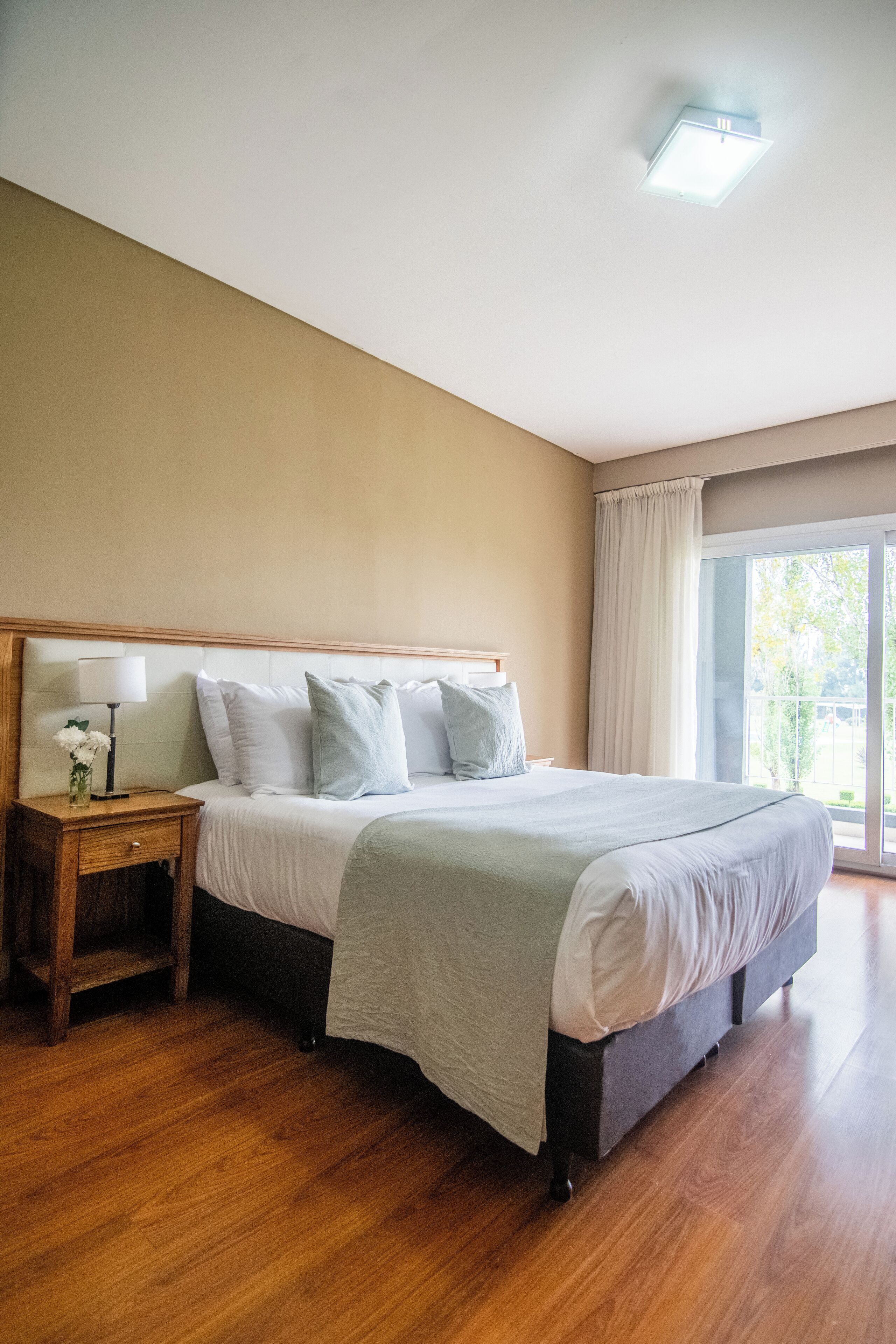 A bedroom with a large bed, wooden nightstand, and a window with curtains.