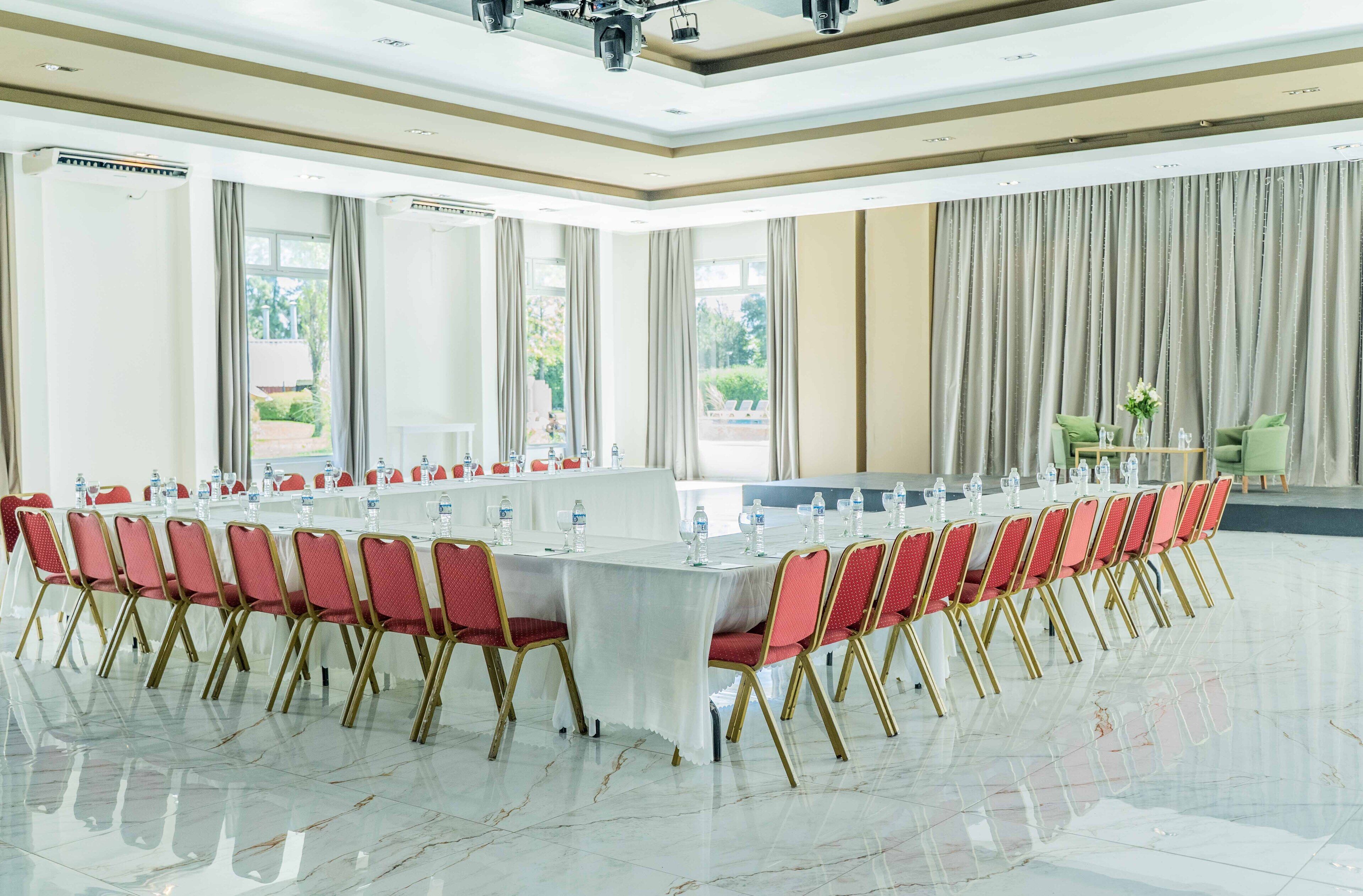 A conference room with a long table, red chairs, and a view of a garden through large windows.