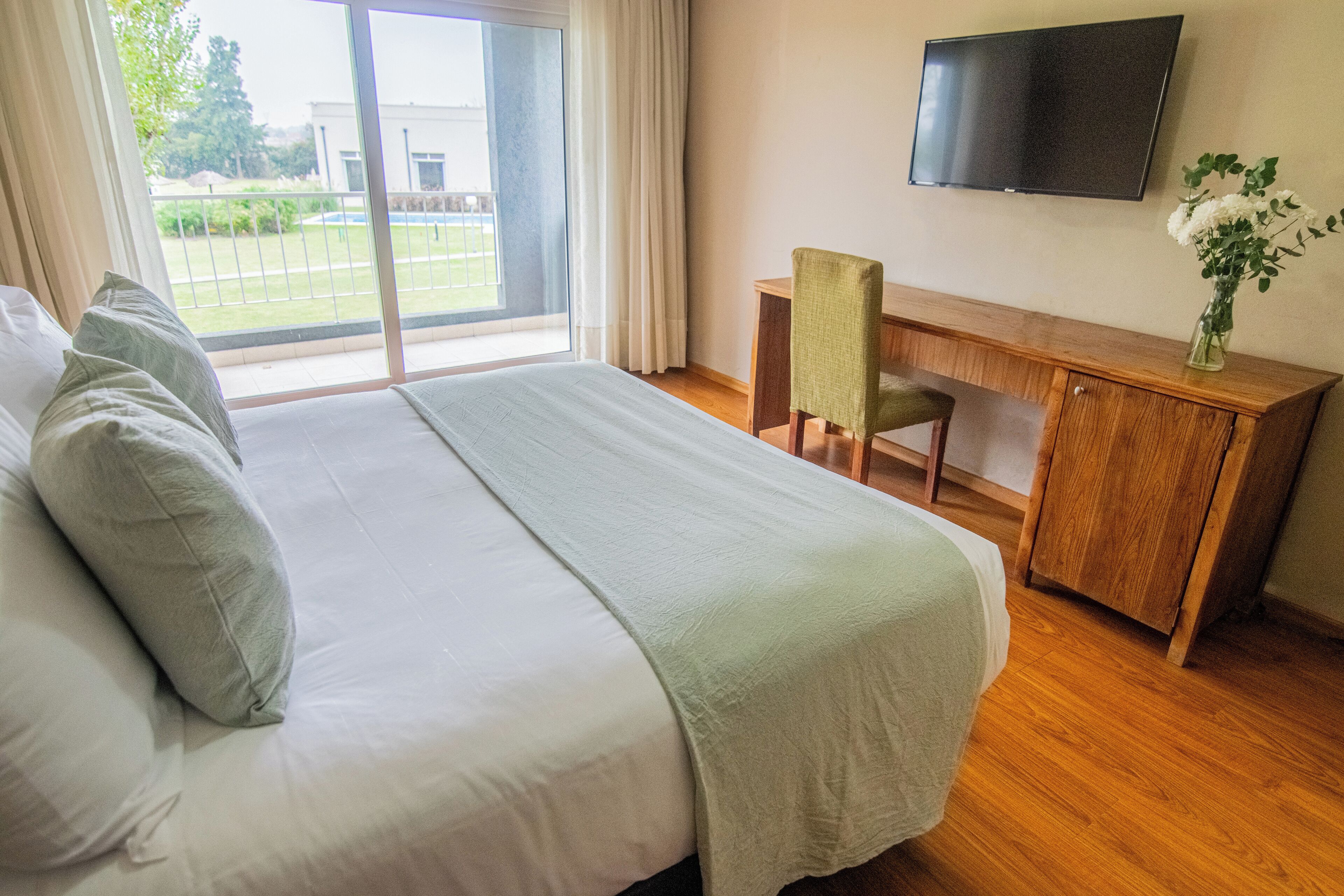 Habitación de hotel con una cama grande, un escritorio con silla, un televisor y vistas al exterior.