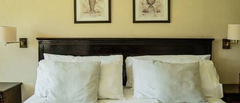 A neatly made bed with white linens and pillows, a dark wooden headboard, and two framed artworks on the wall.