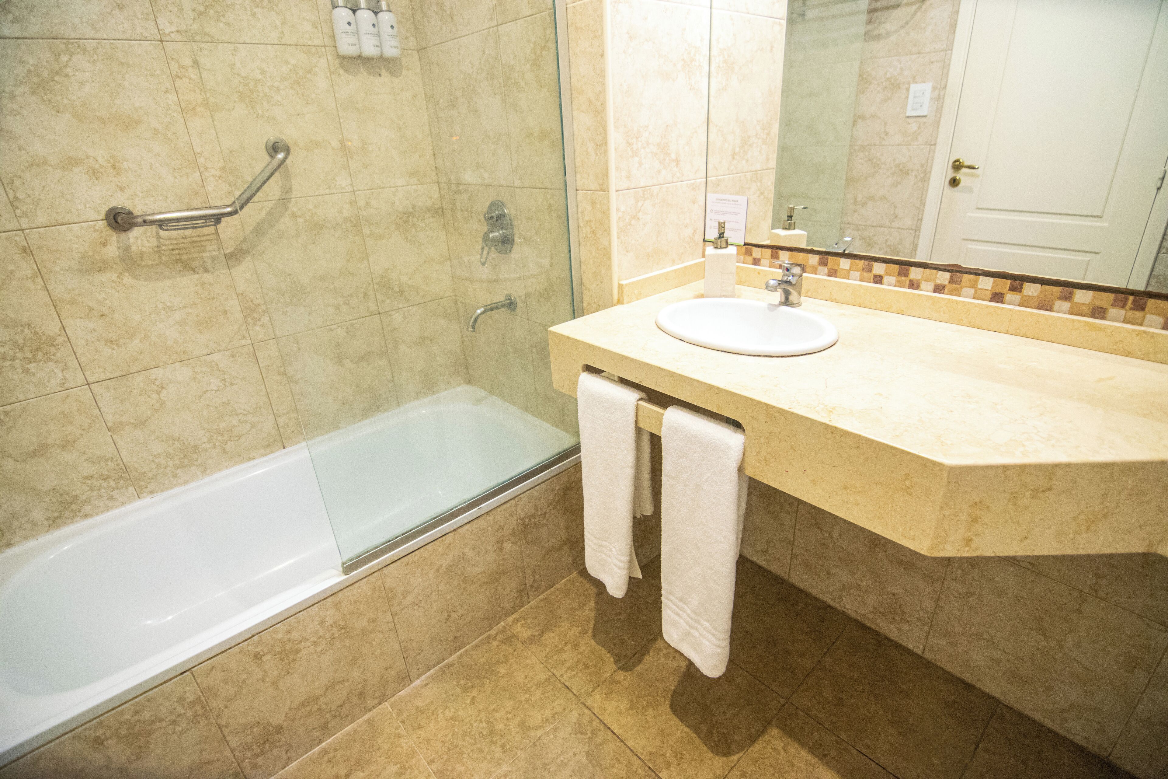 A bathroom with a bathtub, a sink, a handrail, and a mirror.