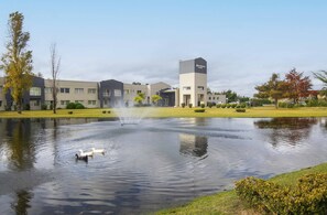 A modern building with a tower labeled 'Wyndham Garden,' a pond with ducks, and a fountain. - Wyndham Garden Campana (Campana)