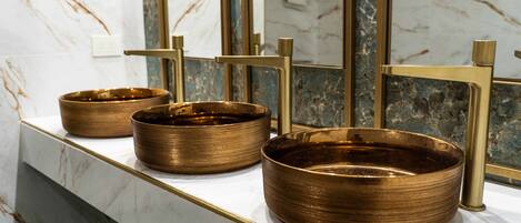 A bathroom with marble countertops and three gold-colored basins.