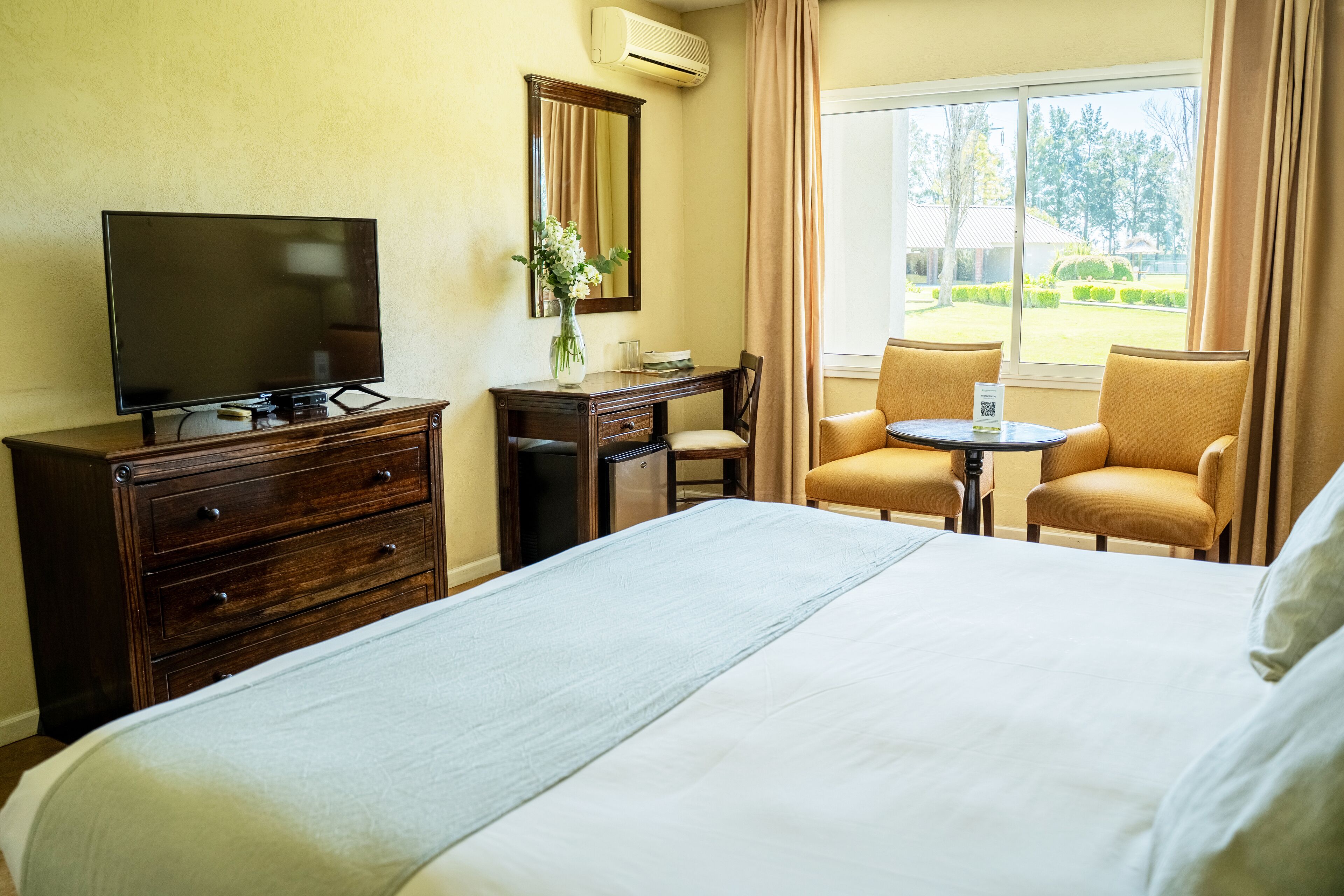 Una camera d'albergo con un letto, una televisione, una scrivania con una sedia e una finestra vista all'esterno.