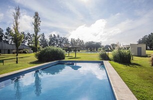 Una piscina con superficie azul cristalina, rodeada de césped cuidado y árboles.