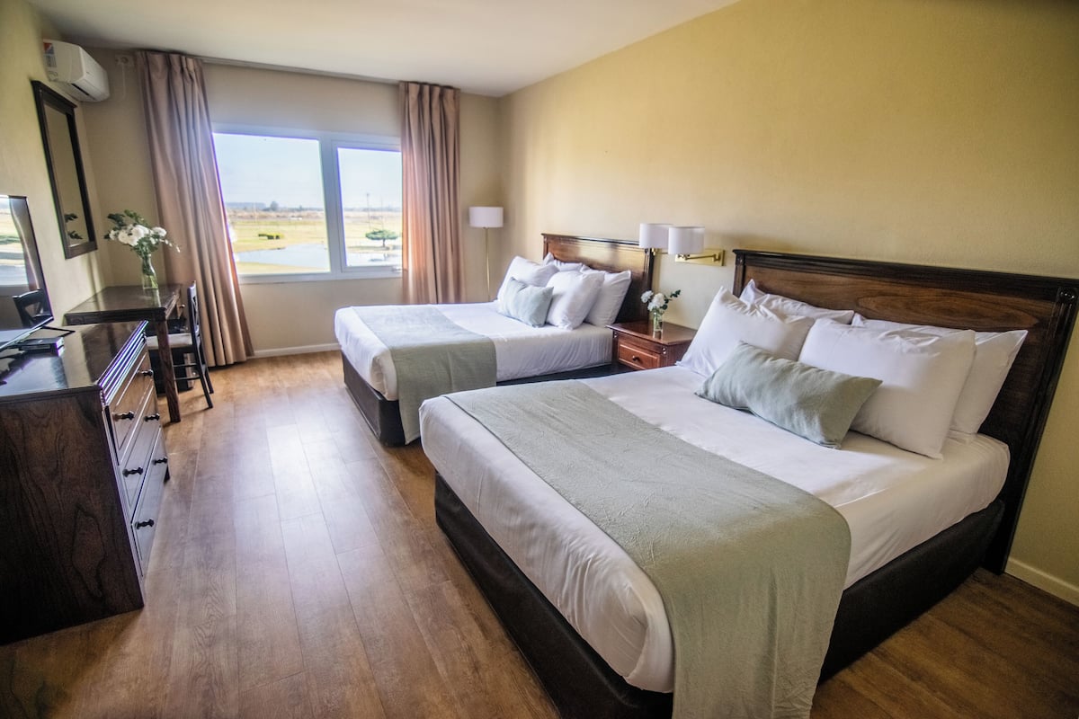 A hotel room with two beds, a desk, and a view of the outdoors.