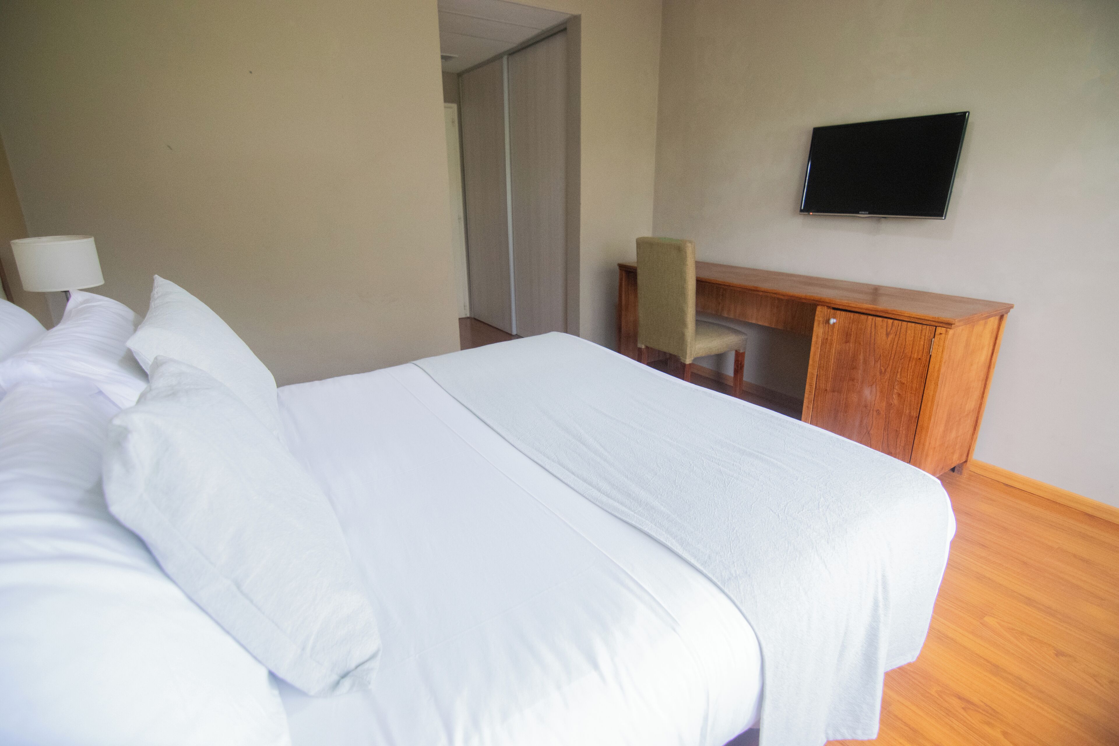 Habitación de hotel con una cama grande, un escritorio, una silla y un televisor de pantalla plana en la pared.