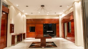 A modern hotel lobby with a central table, wooden paneling, and a unique ceiling light fixture. - San Nicolas Plaza Hotel (San Nicolas de los Arroyos)