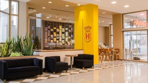 A hotel lobby with a reception desk, seating area, and a large yellow pillar with a crest. - San Nicolas Plaza Hotel (San Nicolas de los Arroyos)