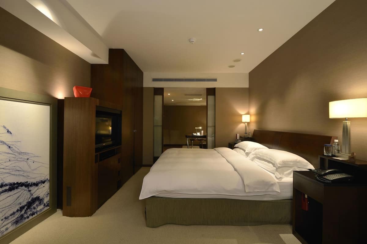 A hotel room with a bed, bedside table, lamp, and a TV.