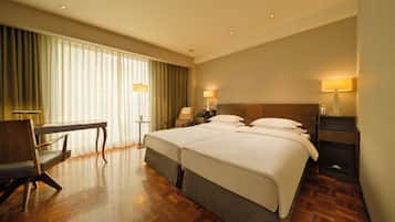 A hotel room with two beds, a desk, a chair, and a lamp.