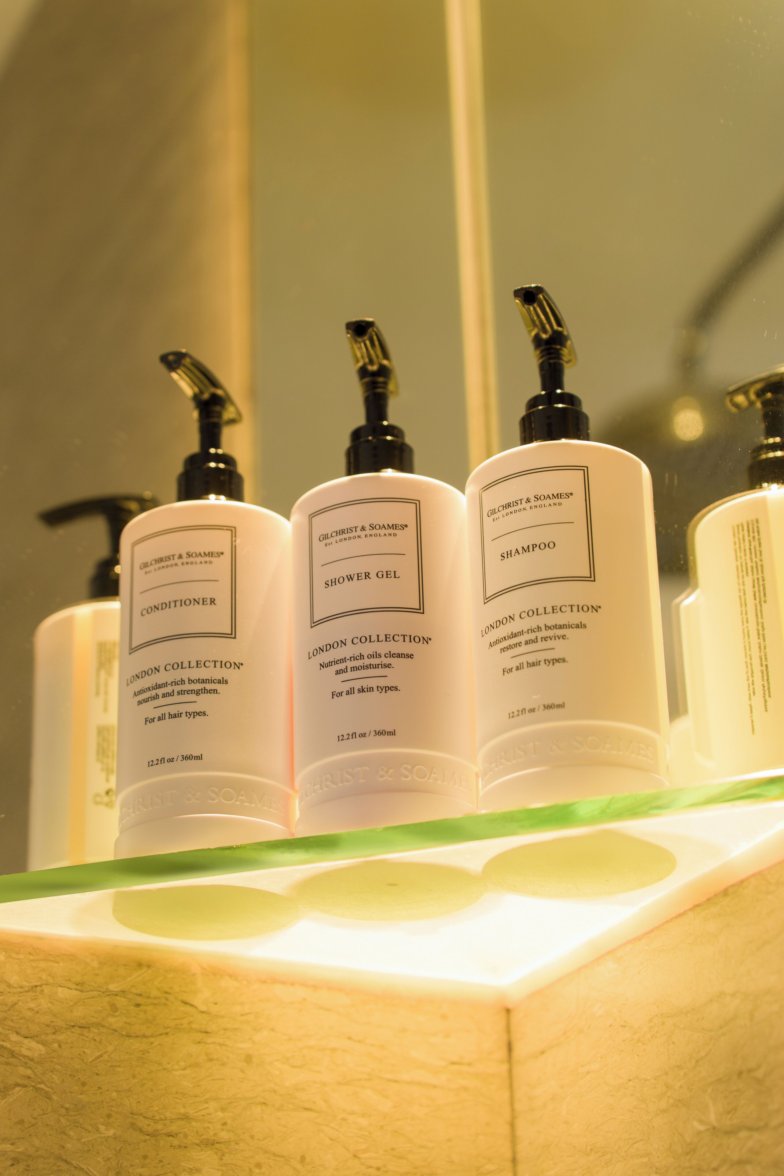 A bathroom shelf with three bottles of London Collection products: conditioner, shower gel, and shampoo.