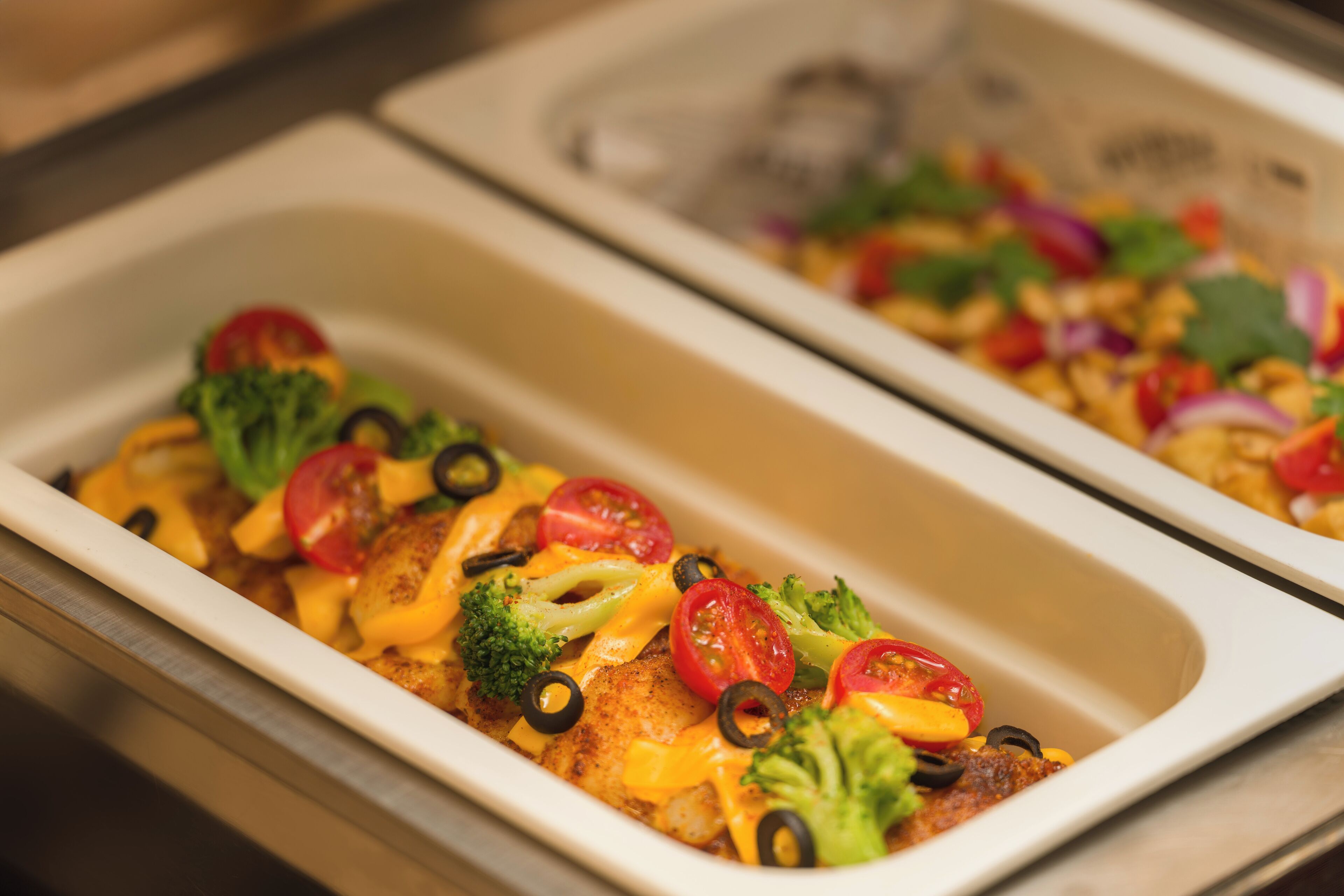 A buffet with a variety of dishes, including a chicken dish with cheese, broccoli, and tomatoes.