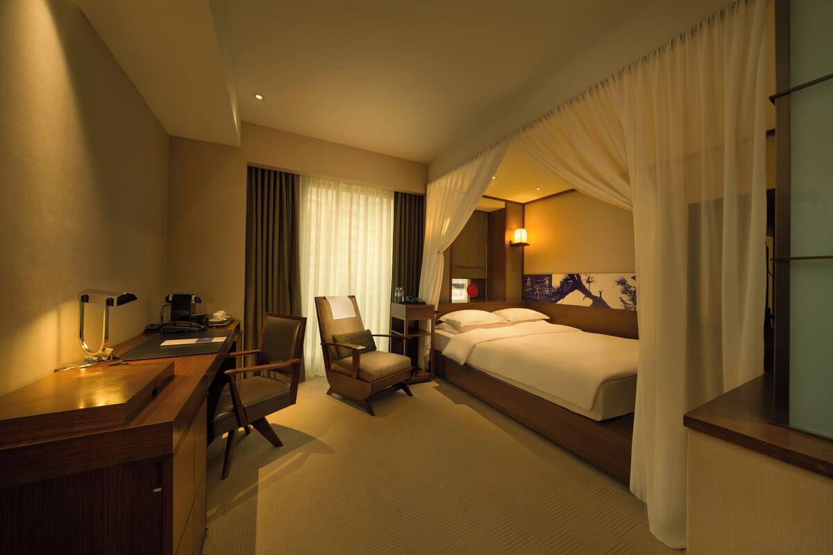 A hotel room with a bed, a desk, a chair, and a nightstand.