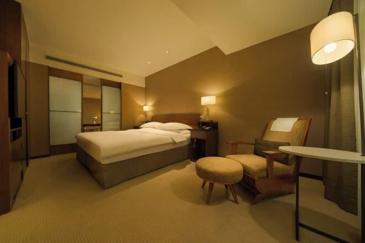 A hotel room with a bed, bedside tables, a chair, a table, and a mirror.
