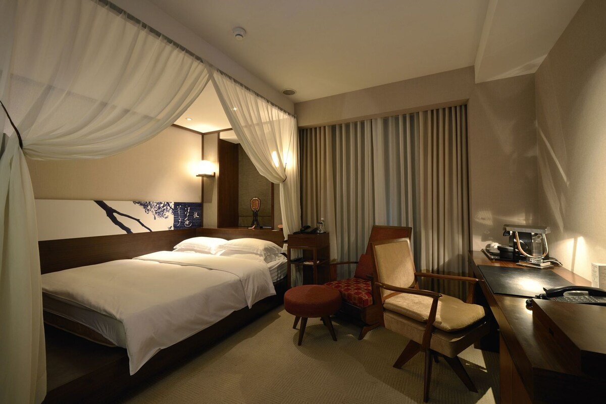 A hotel room with a bed, a desk, a chair, and a window with curtains.