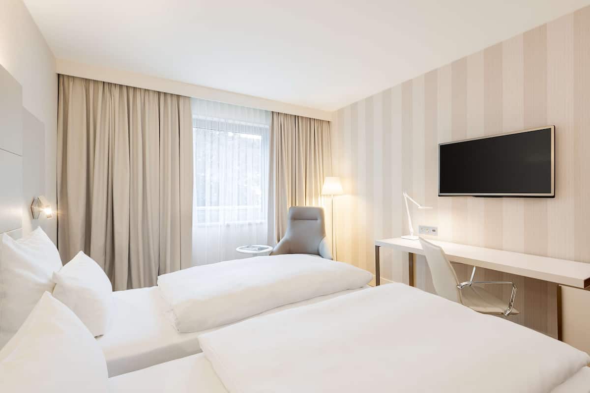 A hotel room with two beds, a desk, a chair, a TV, and a window with curtains.