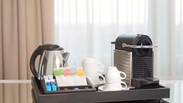 Una cafetera con una bandeja de tazas de café, una jarra y cápsulas de café sobre una mesa.