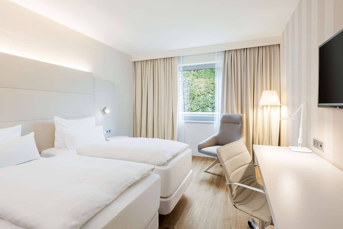 A hotel room with two beds, a desk, a chair, a TV, and a window with curtains.