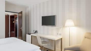 Una habitación de hotel con una cama, un escritorio con una silla, un televisor y una lámpara.