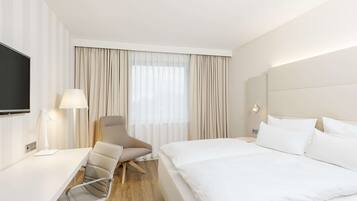 Habitación de hotel con cama, escritorio, silla, televisión y ventana con cortinas.
