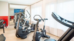 A gym with various cardio machines, a mirror, and a red wall.