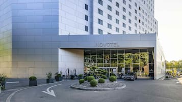 Un hôtel moderne doté d’une façade en verre, d’une entrée dégagée et d’un espace paysager agrémenté d’arbustes soigneusement taillés.