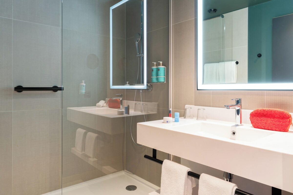 A modern bathroom with a glass shower enclosure, a white sink, and a large mirror.