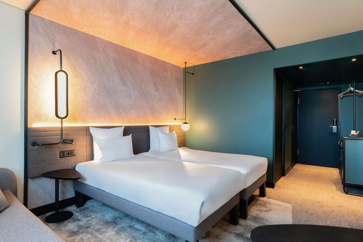 Quarto de hotel moderno com uma cama grande, mesas de cabeceira, uma escrivaninha e um guarda-roupa.