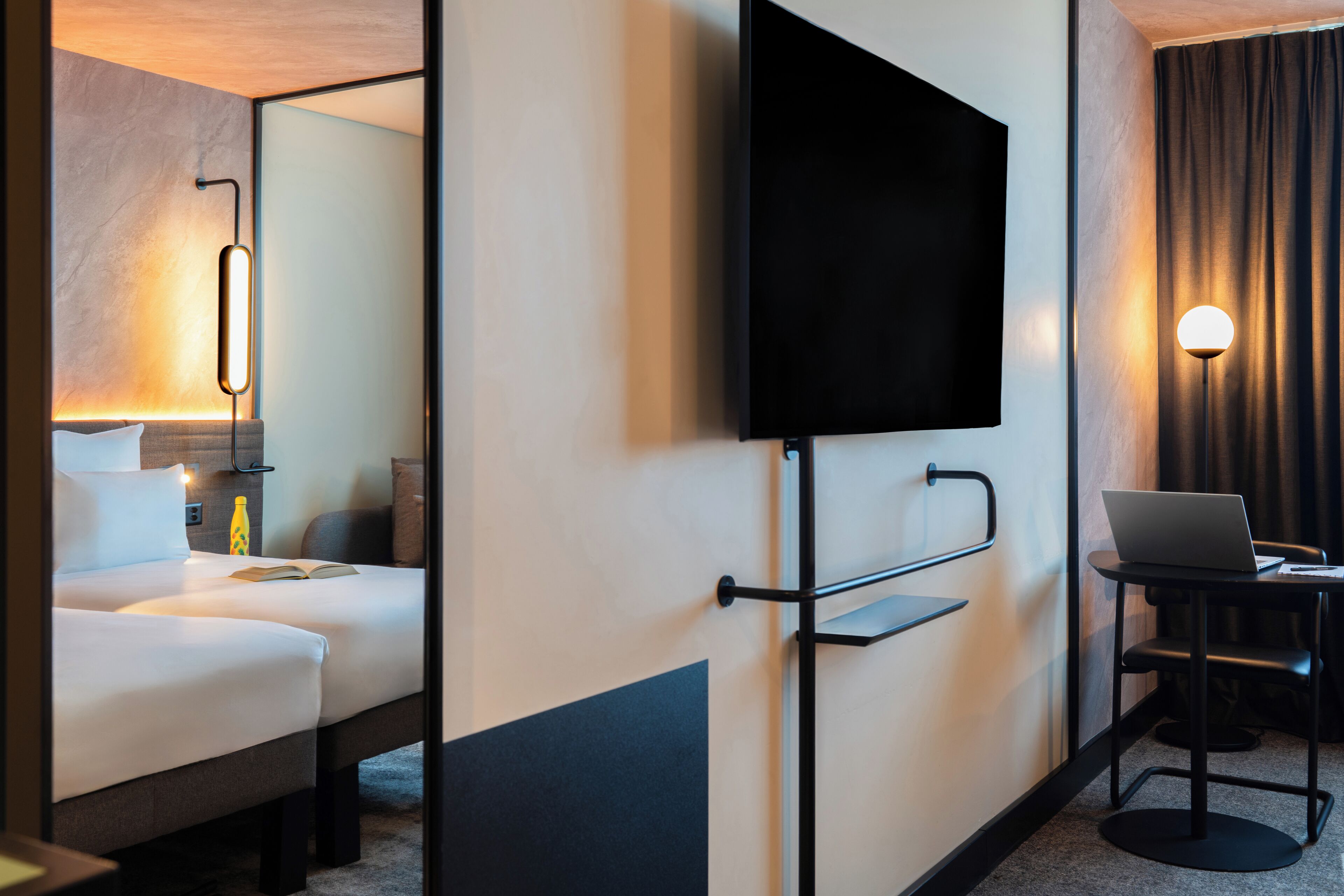 Habitación de hotel con cama, un televisor de pantalla plana en la pared, un escritorio con una computadora portátil y una lámpara.