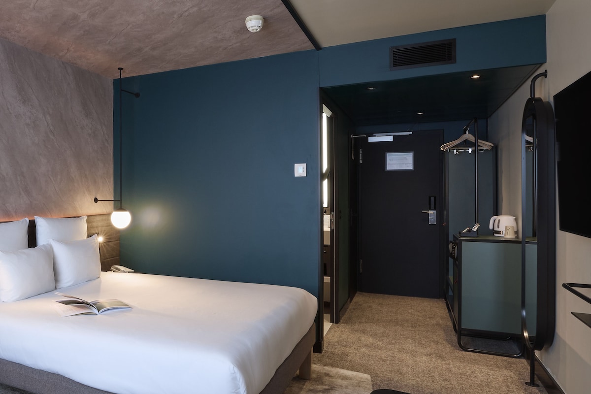A hotel room with a bed, bedside table, and a small table with apples.