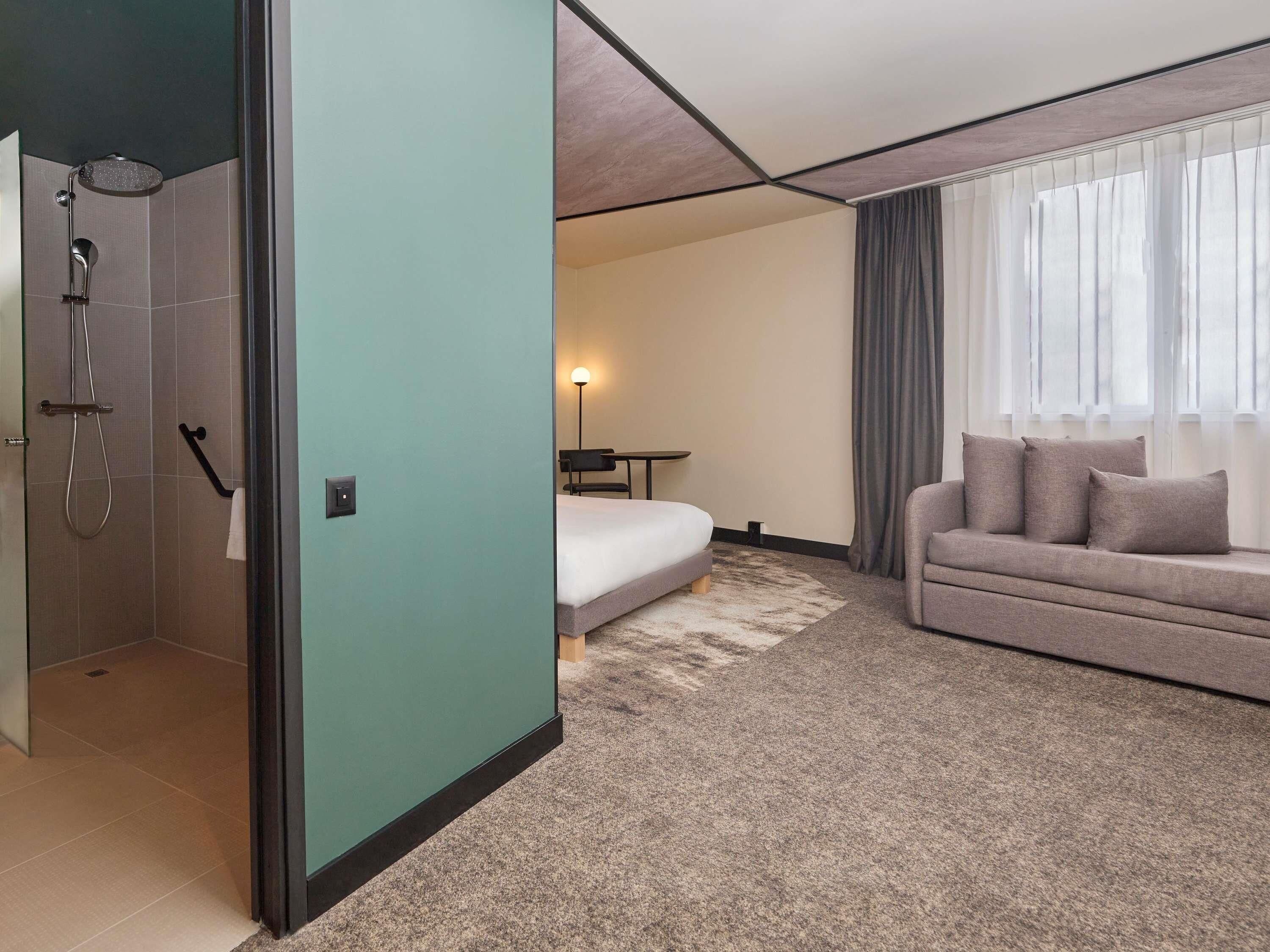 A modern hotel room with a shower, a bed, a sofa, and a small table.