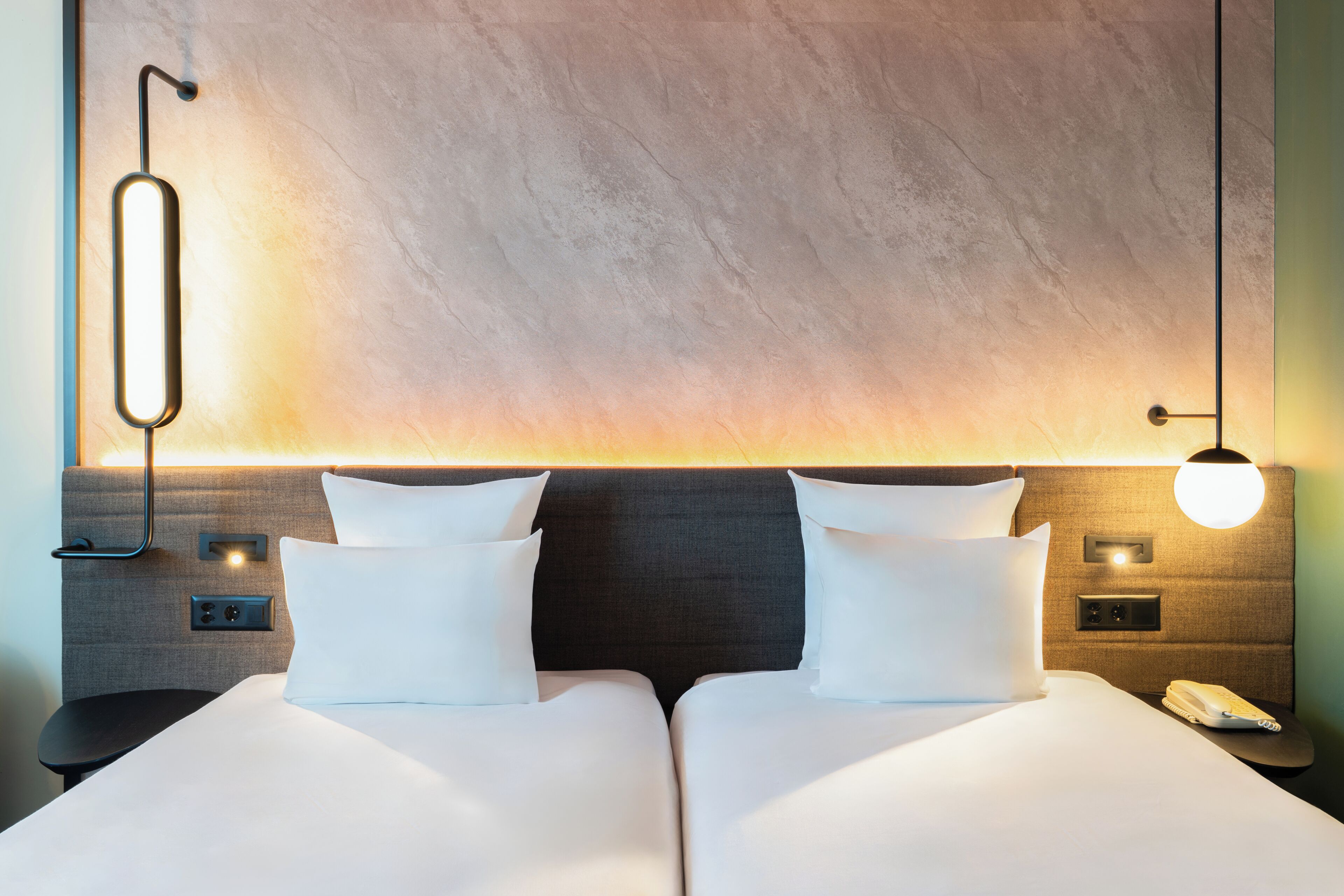 Ett hotellrum med en stor säng, två sängbord, en väggmonterad lampa och en telefon på nattduksbordet.