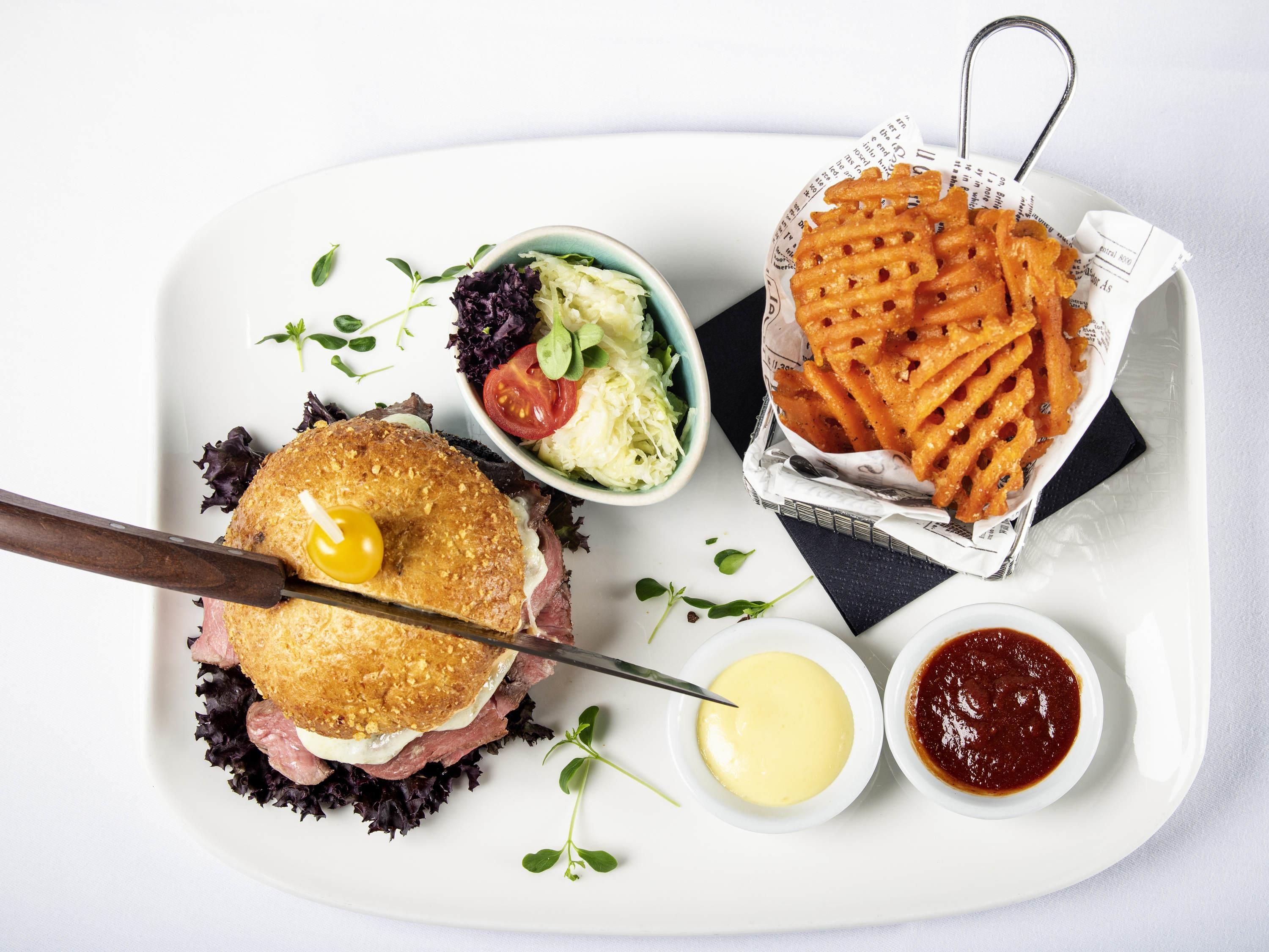 A meal consisting of a sandwich, fries, coleslaw, and condiments on a white plate.